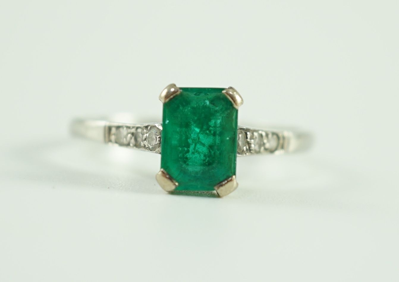 A white gold and single stone emerald ring, with six stone diamond set shoulders